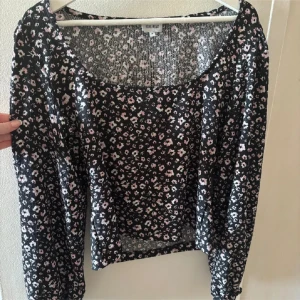 Svart blommig topp från Bubbleroom - Säljer en svart långärmad topp från Bubbleroom med små rosa och vita blommor. Toppen har rund halsringning och är tillverkad i ett lätt ribbat material. 
