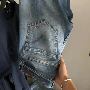 Blå jeansbyxor med normal passform - Säljer ett par klassiska blå jeansbyxor med normal passform och raka ben. Jeansen har fem fickor, snygga slitningar och en lätt tvättad look. Perfekta för en avslappnad stil och passar till det mesta.