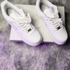 Nike Air Force 1 vita sneakers - Klassiska helvita Nike Air Force 1 sneakers med snörning och rund tå. Skorna har en platt sula och är tillverkade i skinn med diskreta detaljer. Perfekta för dig som gillar en clean och tidlös stil.