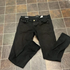 Svarta slim jeans från Jack & Jones - Svarta jeans från Jack & Jones, modell Glenn Slim. Klassisk femficksdesign med dragkedjegylf och knapp. Jeansen har en smal passform och är tillverkade i ett stretchigt material för extra komfort.