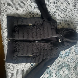 Moncler Cardigan  - Säljer en cardigan från Moncler med huva och dragkedja framtill. Jackan har två fickor med dragkedja och ribbade muddar vid ärmslut och nederkant. Perfekt för kyligare dagar. Den blev köpt i Rumänien i 2023 