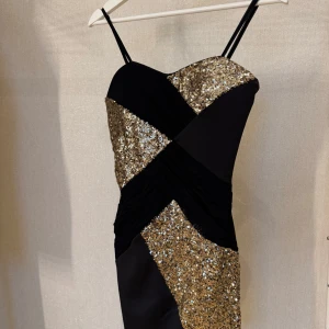 Svart och guldig paljettklänning från Sisters Point - Säljer en snygg svart klänning från Sisters Point i storlek XS. Klänningen har smala axelband och är dekorerad med glittriga guldpaljetter i ett geometriskt mönster. Perfekt för dig som vill sticka ut med en festlig look!