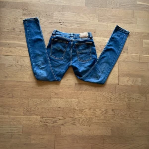 Blå jeans från nudie - Säljer dessa stilrena jeansen från nudie jeans storlek W28 L30 mått brädd midjan 38cm brädd låren 22cm på båda brädd på vaderna 15cm på båda längd 97cm modell straight lin