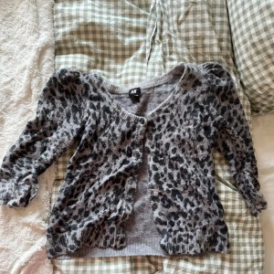 Grå leopardmönstrad kofta från H&M - Säljer en grå kofta med leopardmönster från H&M. Koftan har långa ärmar och knappar framtill. Perfekt för att lägga till lite mönster i din garderob!