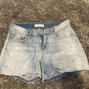 Ljusblå jeansshorts från Denim Union - Ljusblå jeansshorts med klassisk femficksdesign och råa benslut. Shortsen har hög midja och en avslappnad passform, perfekta för varma dagar. Tidlös denimlook som funkar till det mesta.