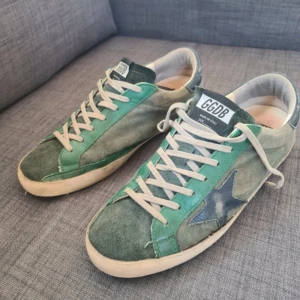 Gröna sneakers från Golden Goose - Säljer ett par gröna Golden Goose sneakers med vit sula och vita skosnören. Skorna har en blå stjärndetalj på sidan och GGDB-logga på plösen. Ovandelen är i mocka och skinn med olika gröna nyanser. Pris kan diskuteras samt tar jag emot byten