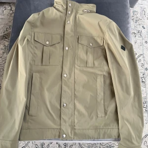 Beige/grön J.Lindberg field jacket  - Säljer nu min J.Lindberg field jacket för jag har växt ur den. Jackan är helt felfri och i 9/10 skick, samt knappar och dragkedjor funkar suveränt. Det är storlek M på jackan men passar även L. Jackan är köpt i butik för 3400 och säljer den nu för 1199. Vid snabb o smidig affär skulle priset kunna diskuteras, tveka inte på att höra av er om ni har frågor eller annat!