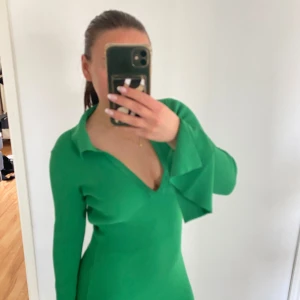 Grön ribbad långklänning med öppen rygg - Säljer en snygg grön ribbad långklänning med djup v-ringning, långa trumpetärmar och öppen rygg. Materialet är stretchigt och följsamt. Från NAKD. Använd 1 gång