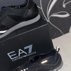 Svarta sneakers från Emporio Armani - Snygga svarta sneakers från Emporio Armani med stilren design. Skorna har snörning och en bekväm sula som ger bra stöd. Perfekta för en trendig och avslappnad look.
