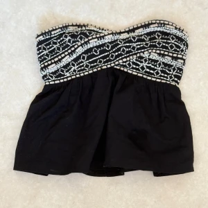 Svart axelbandslös topp från Zara - Snygg svart axelbandslös topp från Zara med ett detaljerat mönster i vitt på överdelen. Perfekt för en ute kvällar!💕