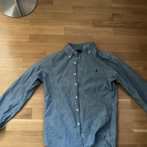 Blå jeansskjorta från Ralph Lauren - Säljer en snygg blå jeansskjorta från Ralph Lauren i slim fit. Skjortan har långa ärmar och knappar framtill. Perfekt för en stilren look. Kommer i väldigt bra skick och i strl M! Skriv för funderingar!