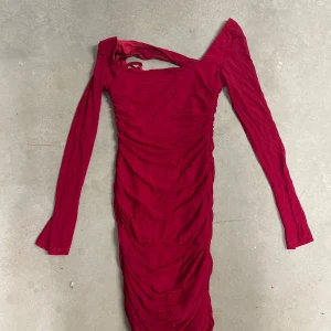 Röd tight långärmad klänning med rynkade detaljer - Säljer en röd långärmad klänning med tight passform och rynkade detaljer längs hela klänningen. Klänningen har en fyrkantig ringning och är tillverkad i stretchigt material av 95% polyamid och 5% elastan. Perfekt för dig som vill sticka ut!