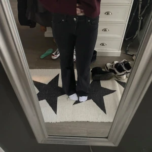 Svarta bootcut jeans - Säljer ett par svarta bootcut jeans med klassisk femficksdesign och knappgylf. Jeansen har en normal passform och är tillverkade i ett stretchigt denimtyg som sitter snyggt över höfterna och släpper ut vid bensluten.