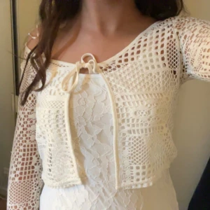 Vit spetsbolero från H&M - Säljer en söt vit spetsbolero från H&M. Den är croppad och har långa ärmar med knytning framtill. Perfekt för att lägga till en romantisk touch till din outfit.