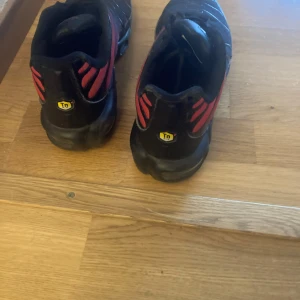 Svarta och röda Nike sneakers (TN) - Säljer ett par svarta och röda Nike sneakers med TN-logga på hälen. Skorna har en sportig design med snörning och en bekväm sula. Perfekta för en casual look eller träning.  Knappt använda. 