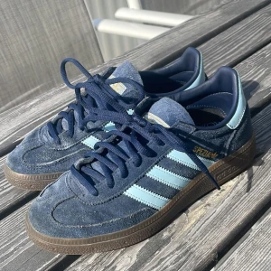 Adidas Spezial sneakers i blå mocka - Säljer ett par Adidas Spezial sneakers i blå mocka med ljusblå ränder och mörkblå snörning. Skorna har klassisk gummisula och guldfärgad Spezial-logga på sidan. Perfekta för dig som gillar retrostil och streetwear.