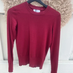 Vinröd tröja  - Vinröd långärmad tröja från Holly & Whyte med rund halsringning och dekorativa knappar vid ärmslutet. Tröjan är i mjukt, tunt stickat material och har en klassisk, enkel design. SKRIV INNAN KÖP! endast använd en gång.❤️