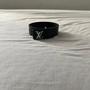 Svart Louis vuitton armband med en silver loga - Stilrent armband i svart läder med silverdetalj inspirerad av Louis Vuitton. Ej äkta – men med exklusiv känsla och grym look! Perfekt för dig som vill lyfta din outfit med en lyxig touch utan att spräcka plånboken. Bekvämt, justerbart och i mycket fint skick. En accessoar som garanterat drar blickar. Pris: 750 kr. 