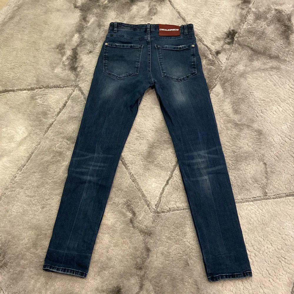 Säljer ett par mörkblå jeansbyxor från Dsquared2 med slitna detaljer framtill och klassisk femficksdesign. Byxorna har rak passform och normal midja. Perfekta för dig som gillar en stilren men ändå trendig look.. Farkut & Housut.