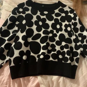 Svartvit blommig stickad tröja från h&m - Säljer en svartvit stickad tröja från h&mmed stora blommiga mönster. Tröjan har lång ärm, rund halsringning och ribbade muddar vid ärmslut och nederkant. Perfekt för att liva upp garderoben med ett statement-plagg!