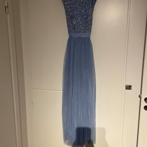 Ljusblå långklänning med paljetter - Säljer en ljusblå långklänning med glittrig paljettöverdel och djup v-ringad rygg. Kjolen är i tunt, flowy tyg som ger en elegant känsla. Perfekt för bal eller fest! 💙