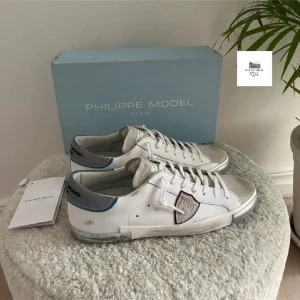 Vita sneakers från Philippe Model med grå detaljer - Säljer ett par snygga Philippe Model skor. Använda men i väldigt bra skick. Nypris runt 3500-4000kr. Box och allt ingår såklart. Väldigt snygga till våren och sommaren. Skriv för funderingar. Pris kan diskuteras vid snabb affär!