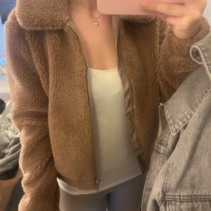 Beige teddyjacka med dragkedja - Mysig beige teddyjacka med dragkedja framtill. Perfekt för vår dagar med sin fluffiga design. Jackan har långa ärmar och en klassisk krage. 