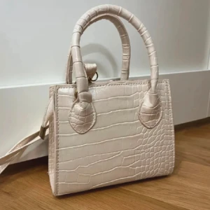 Väska  - Beige väska, med tillhörande band med!   Höjd 15cm och längd 17cm! 