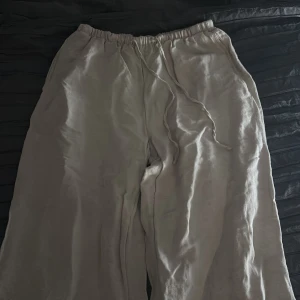 Beiga linnebyxor med dragsko - Säljer ett par beiga linnebyxor med breda ben och resår i midjan samt dragsko. Byxorna är luftiga och perfekta för varmare dagar. Tillverkade i en linnemix som ger en skön känsla mot huden. Har lite defekter vid slutändan på benen bak men inget som syns