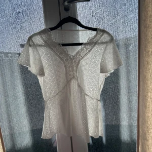 Vit spetsblus med kort ärm - Vit blus med vackra spetsdetaljer och korta ärmar. Blusen har ett diskret mönster och v-ringad halsringning med spetskant. Väldigt söt och passar jätte bra till både jeans och kjol ! Använd fåtal gånger och köpt på marknad i rhodos! 