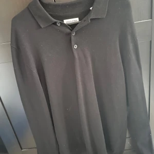 Svart pikétröja från Jack & Jones - Klassisk svart pikétröja från Jack & Jones med krage och två knappar framtill. Tröjan har lång ärm och är tillverkad i ett mjukt material som passar perfekt till många olika tillfällen. Tröjan är helt ny och aldrig använd.🍾