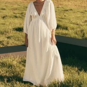 Vit långklänning med v-ringning - Elegant vit långklänning med djup v-ringning och puffiga långa ärmar. Perfekt för sommarens festligheter. Klänningen har en luftig passform och är tillverkad i ett lätt material som ger en skön känsla. Från Cubus. Använd en gång, mycket bra skick. 