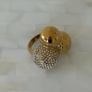 Guldfärgad ring med stenar - Snygg guldfärgad ring med tre stora kulor, varav en är täckt med glittrande stenar. Perfekt för att ge en extra touch av glamour till din outfit. Guld plågering med stainless steel 🤍