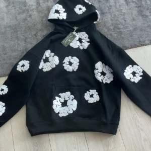  Denim Tears tröja - Säljer en svart hoodie från Denim Tears med unika vita mönster över hela plagget. Hoodien har en klassisk passform med en stor ficka framtill och en bekväm huva. Perfekt för en stilren och avslappnad look.