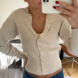 Slutsåld kofta och linne från Zara! - Trendig beige kofta med ribbad midja och långa ärmar. Koftan har en croppad passform och knappar längs hela framsidan. Perfekt att styla med jeans eller kjol för en snygg vardagslook. Till får du även ett linne som sitter ihop med koftan perfekt ihop!! Men även isär!! Köpte för 700!