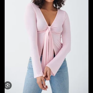 Ljusrosa långärmad topp med knyt - Säljer en ljusrosa långärmad topp med djup v-ringning och knyt framtill. Toppen har en croppad passform och är tillverkad i mjukt bomullsmaterial. Perfekt att styla med jeans eller kjol. Färgen ser off ut på bild men är inte de i verkligheten storlek S