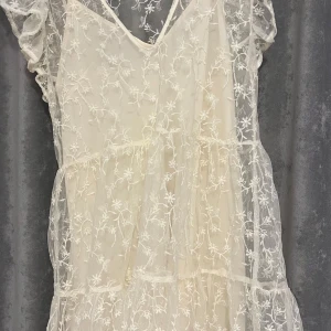 Vit blommig spetsklänning från Zara - Superfin vit klänning från Zara i spets med blommigt mönster. Klänningen har volangdetaljer och är ärmlös med v-ringning. Perfekt för sommarens tillfällen och ger en romantisk look.