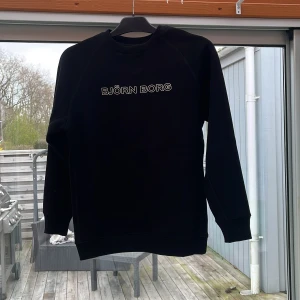 Svart sweatshirt från Björn Borg - Säljer en svart sweatshirt från Björn Borg med vit logotyp på bröstet. Tröjan har rund halsringning och långa ärmar. Perfekt för en avslappnad och sportig stil. Ny utan prislapp, utmärkt skick! Storlek 158/164