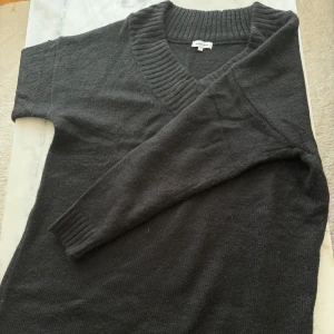 Svart kort stickad klänning från BubbleRoom - Svart kort stickad klänning från BubbleRoom med bred v-ringning och långa ärmar. 