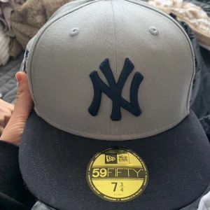 Grå keps från New Era - Säljer en stilren grå keps från New Era med mörkblått broderat emblem framtill.  Helt ny. 