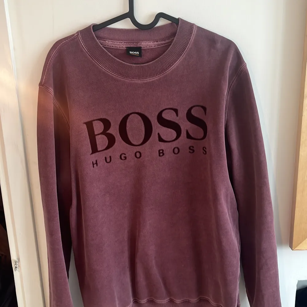 Säljer en stilren vinröd tröja från Hugo Boss med deras logga tryckt på framsidan. Tröjan har långa ärmar och en rund halsringning med ribbade kanter. Perfekt för en avslappnad och trendig look.. Neuletakit & Villapaidat.
