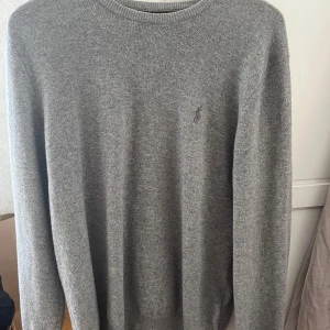 Grå tröja från Polo Ralph Lauren - Säljer en stilren grå tröja från Polo Ralph Lauren. Tröjan har en klassisk rund hals och är långärmad. Den är tillverkad i ett mjukt material och har en diskret logga på bröstet. Perfekt för en avslappnad och snygg look.