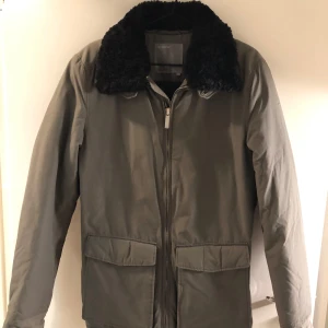 Grön J.Lindeberg jacka med fuskpälskrage - Snygg grön jacka med svart krage från J.Lindeberg Jackan har en dragkedja framtill och två stora fickor. Perfekt för kyligare dagar med sin stilrena design.