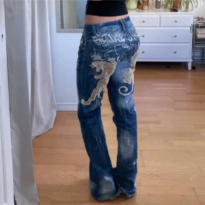 Blå jeans med lejonbroderi - Unika blå jeans med stort lejonbroderi i guld på baksidan. De har en lågmidjad passform och slitna detaljer för en cool look. Perfekta för dig som vill sticka ut!