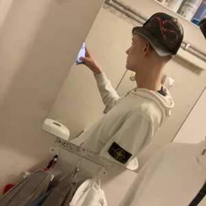 Vit hoodie från Stone Island - Säljer en stilren vit hoodie från Stone Island med dragkedja och deras ikoniska märke på ärmen. Perfekt för en casual look. Den har en bekväm passform och är långärmad.