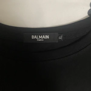 Svart t-shirt från Balmain - Säljer en stilren svart t-shirt från Balmain med vit logotyp på bröstet. T-shirten har en klassisk passform och är kortärmad. Perfekt för en trendig och avslappnad look.