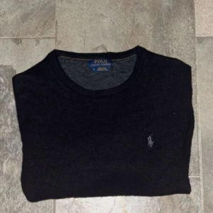 Polo tröja 100% merino ull - Säljer en stilren svart tröja från Polo Ralph Lauren med det klassiska broderade logotypen på bröstet. Tröjan har långa ärmar och en rund halsringning. Perfekt för en avslappnad och snygg look.100% merino ull