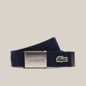 Blått bälte från Lacoste - Snyggt blått bälte från Lacoste med en stilren silverfärgad spänne. Bältet har den ikoniska krokodilloggan broderad på sidan. Perfekt för att ge en sportig touch till din outfit.