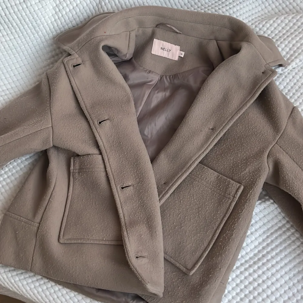 Säljer en snygg och skön beige kappa från Nelly. 💗Jättebra skick! Jackan har en klassisk design med stora fickor och knappar framtill och längst ner på ärmen. Perfekt för höst och vår, med en mjuk och bekväm passform. Säljer eftersom att den bara kommit till användning cirka 3-4 gånger. Kappan är som ny, bara att den har blivigt lite knopprig, men det blir alla kappor nästan direkt. OBS: den ser brun ut på andra bilden men är BEIGE. 🙌🏽💞 pris kan diskuteras privat. . Takit.