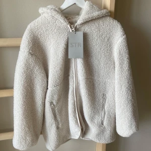 Vit teddyjacka med huva - Mysig vit teddyjacka från stradivarius med huva och dragkedja framtill. Jackan har två fickor med dragkedjor och är perfekt för kyligare dagar. Den är väldigt bekväm och fin men var tyvärr inte i min storlek och kunde inte returnera🩷 nypris 430kr, går att ha som kofta också